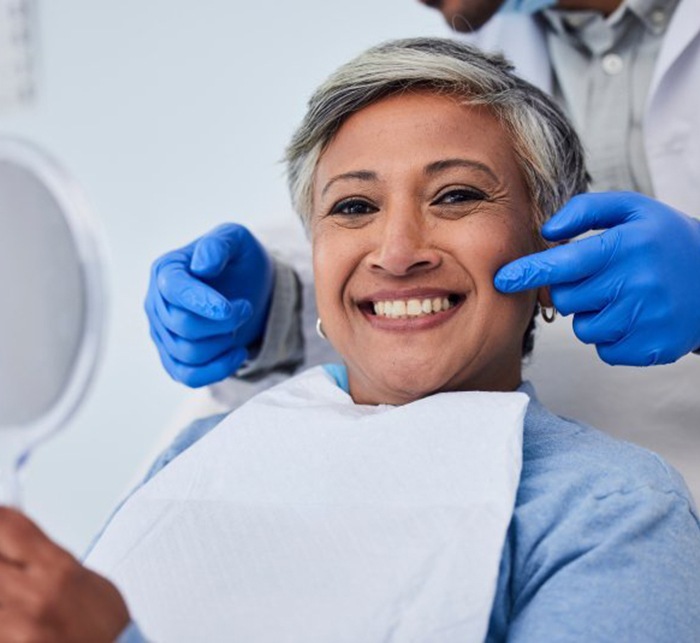 a patient smiling while checking her teeth with a mirror