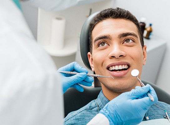 Man in denim shirt smiling at dentist about to examine his teeth