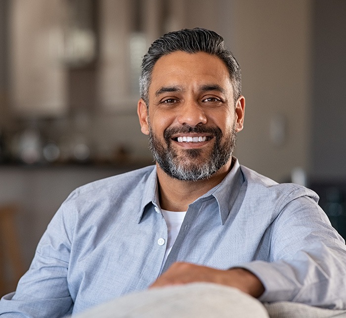 Middle-aged man on couch and smiling after root canal treatment in White Marsh