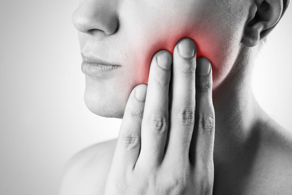 a person holds the side of their mouth in pain and wonders about wisdom teeth removal cost