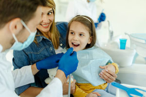 a young child sits in a dentist's exam chair and receive an orthodontic treatment from dentist