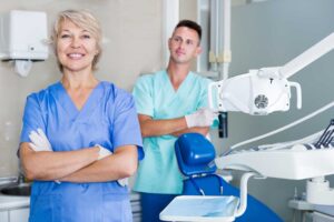 a dental assistant and a emergency dentist stand together with their arms crossed while in a dental exam room