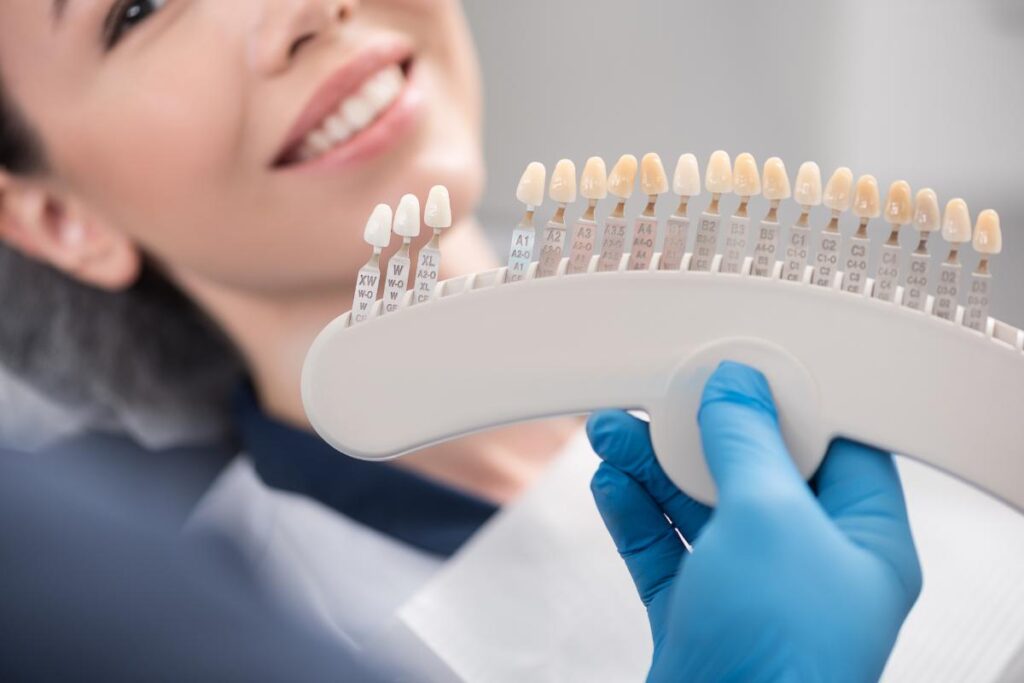 a dentist holds up an assortment of veneer shades to smiling patient to get the right match and answers patients question about are porcelain veneers worth it