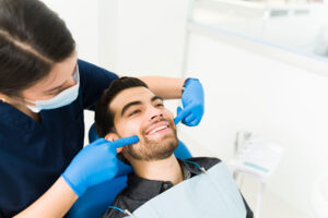 a dental professional works on a patients teeth and explains to him why its important for routine dental visits